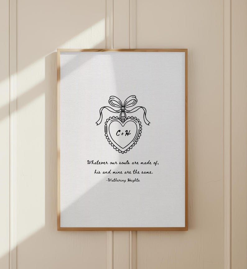 A framed print with a wooden frame. The print features a heart-shaped design with the initials "C+H" inside, adorned with a bow and ribbon. Below the design is a quote from Wuthering Heights.