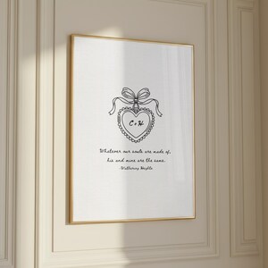 A framed print with a gold border, featuring a black line drawing of a heart with a bow and the initials "C+H". The text reads "Whatever our souls are made of, his and mine are the same. Wuthering Heights."