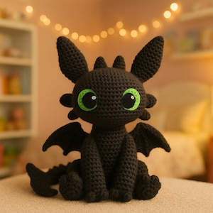 May include: A handmade black crochet dragon with large green eyes, small wings, and a long tail. The dragon is sitting on a neutral surface. The background is softly lit with string lights, suggesting a cozy setting. This plush toy is perfect for children.