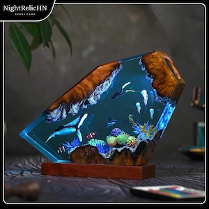 May include: A decorative epoxy lamp featuring an underwater scene with a whale, fish, and coral. The lamp has a wooden base and a clear resin body with a blue glow. The top of the lamp has a wood grain design. The text "NightRelicHN EPOXI LAMP" is in the upper left corner.