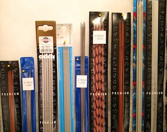 Puede incluir: Una colección de agujas de tejer de varios tamaños y colores, incluyendo plata, cobre y madera. Las agujas están empaquetadas en plástico transparente y etiquetadas con su tamaño en milímetros y tamaño estadounidense. Las etiquetas también incluyen las marcas "Addi" y "Milward".