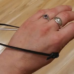 May include: A black strap with a metal rod attached to it. The strap is wrapped around a person's wrist.