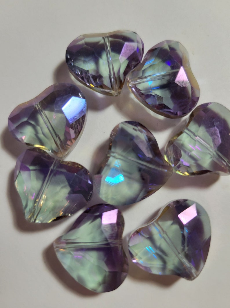 May include: A cluster of iridescent heart-shaped beads. The beads are faceted, reflecting a range of colours including purple, green, and blue. These decorative beads are suitable for jewellery making and craft projects.