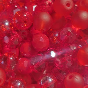 May include: A close-up of a collection of red beads. The beads vary in shape and texture, including faceted, round, and matte finishes. The color is a vibrant, saturated red, with light reflecting off the surfaces.