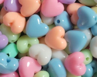 May include: A collection of pastel-colored heart-shaped plastic beads. The beads are in various shades of pink, blue, green, and yellow.