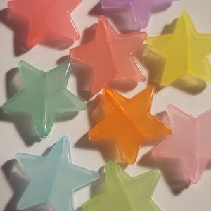 May include: A collection of translucent star-shaped objects in various colors, including red, purple, yellow, green, orange, and blue. The stars are evenly spaced and appear to be made of plastic or a similar material.