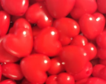 May include: A close-up image of a pile of red heart-shaped beads. The beads are smooth and shiny, and they are all the same size.