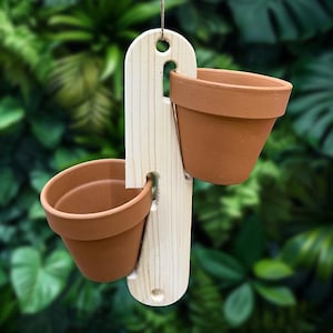 May include: A hanging planter with two terracotta pots held by a light-coloured wooden frame. The frame has a curved top with a hole for hanging and slots to hold the pots. The pots are empty and ready for planting.