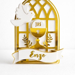 Pode incluir: Topper de bolo de comunhão dourado e branco com pomba, cálice e design de janela arqueada. A faixa exibe o nome "Enzo" em escrita dourada. O topper é feito de papel em camadas.