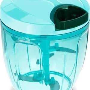 May include: A teal and white manual food chopper. The chopper has a clear, transparent container with a teal lid and handle. Inside, there are blades attached to a central mechanism. A small black button is on top of the lid.