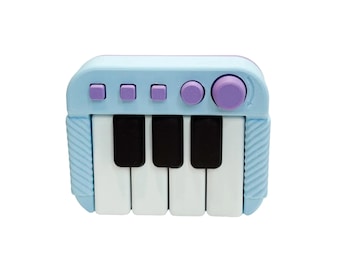 May include: A miniature toy piano in shades of light blue, white, and black. The keys are white and black, with light blue buttons and a purple knob. The sides have a ribbed texture.