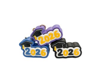 May include: Three graduation-themed keychains in blue, purple, and black. Each keychain features the year "2026" in yellow with a graduation cap. The keychains are on a white background.