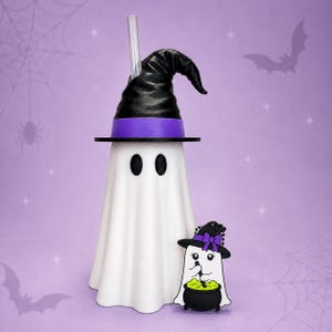 May include: A white ghost-shaped tumbler with a black witch hat lid and a clear straw, accompanied by a small ghost-shaped charm featuring a white ghost wearing a black hat with a purple bow, stirring a green liquid in a black cauldron.