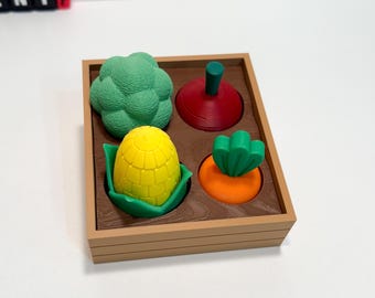 May include: A wooden tray filled with colorful, 3D-printed vegetables. The tray contains a green broccoli, a red beet, a yellow corn on the cob, and an orange carrot. The vegetables are designed to fit snugly within the tray's compartments.