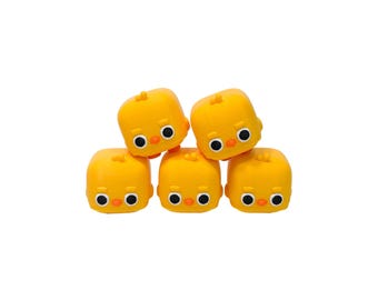 May include: Five yellow, cube-shaped chick figurines with black and white eyes and orange beaks are stacked on top of each other. The figurines have a smooth, matte finish and are arranged against a white background.