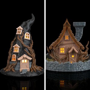 May include: Two decorative house figurines with internal lighting. The left is a tall, black, pointed structure with tree-like textures. The right is a brown, wood-textured cottage with a stone chimney and a surrounding low stone wall.