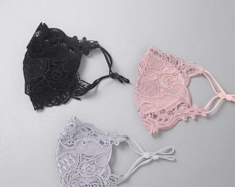 May include: Three face masks featuring intricate floral lace patterns in black, soft pink, and light gray. Each mask includes adjustable elastic ear loops with small plastic toggles to secure the fit, showcasing detailed embroidery and scalloped edges.