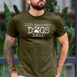 K&ouml;nnte beinhalten: Olivgr&uuml;nes T-Shirt mit dem Text "life happens DOGS help" in verblichener wei&szlig;er Schrift. Das Wort "DOGS" zeigt einen Pfotenabdruck. Das Shirt ist kurz&auml;rmelig und aus weichem Material.