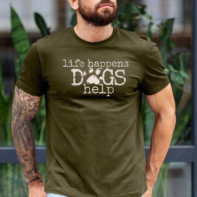 K&ouml;nnte beinhalten: Olivgr&uuml;nes T-Shirt mit dem Text "life happens DOGS help" in verblichener wei&szlig;er Schrift. Das Wort "DOGS" zeigt einen Pfotenabdruck. Das Shirt ist kurz&auml;rmelig und aus weichem Material.