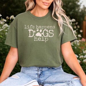 K&ouml;nnte beinhalten: Olivgr&uuml;nes T-Shirt mit dem Text "life happens DOGS help" in verblichener wei&szlig;er Schrift. Das Wort "DOGS" hat ein Pfotenabdruck-Design. Das Shirt ist kurz&auml;rmlig und hat einen Rundhalsausschnitt.