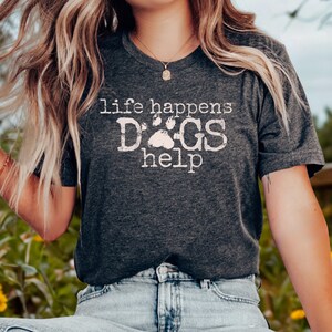 K&ouml;nnte beinhalten: Dunkelgraues T-Shirt mit dem Text "life happens DOGS help" in verblichener wei&szlig;er Schrift. Das Wort "DOGS" ist mit einem Pfotenabdruck-Design versehen. Das Shirt besteht aus einem weichen Material.