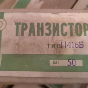 May include: A rectangular cardboard box with a white and green label. The label features the Cyrillic text "ТРАНЗИСТОР" in green, followed by "тип П416Б" in black and blue, and the number "50" printed in blue ink on a white rectangular background.