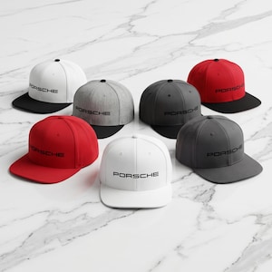 May include: A collection of six baseball caps featuring the Porsche logo in black text on the front. The caps are available in various colors including white with a black brim, solid red, solid white, heather gray, and two shades of dark gray.