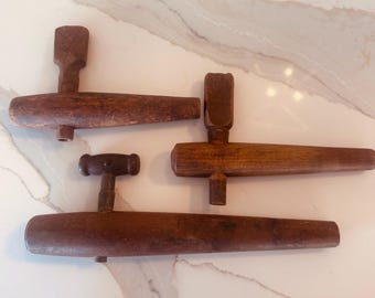 Peut inclure: Trois robinets de tonneau en bois vintage disposés en groupe. Chaque robinet présente un long corps cylindrique effilé avec une poignée perpendiculaire sur le dessus et un petit bec s'étendant vers le bas. Le bois montre un grain brun naturel.