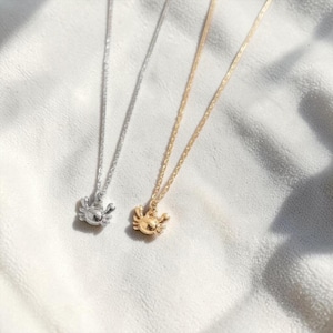 May include: Two necklaces with crab pendants. One necklace is silver, the other is gold. The crab pendants are detailed and have small claws. The necklaces are on a white, textured surface.