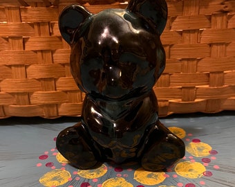 May include: A black ceramic bear figurine with a glossy finish. The bear is sitting with its paws in front of it. The bear is on a blue surface with yellow and pink polka dots.