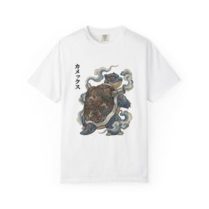 Puede incluir: Camiseta blanca con una ilustración detallada de una criatura parecida a una tortuga con un caparazón estampado, rodeada de humo estilizado. Texto japonés impreso verticalmente en el lado izquierdo.