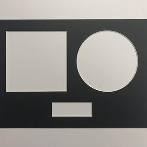 May include: A black picture mount with three apertures: a square, a circle, and a rectangle. The apertures are white, contrasting with the black mount. Designed for displaying multiple photos or artwork.