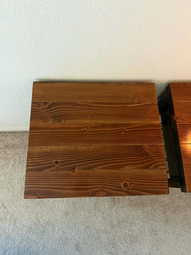 K&ouml;nnte beinhalten: Zwei Nachttische aus Holz mit dunkler brauner Beize. Die Tische sind rechteckig mit sichtbarer Holzmaserung und Knoten, was auf einen rustikalen Stil hindeutet. Die Tische stehen auf einem hellen Teppich.