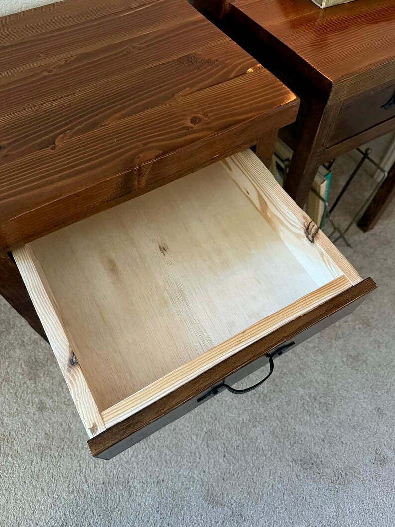 K&ouml;nnte beinhalten: Nahaufnahme eines Nachttisches aus Holz mit ge&ouml;ffneter Schublade. Der Nachttisch ist dunkelbraun gebeizt, mit sichtbarer Holzmaserung. Die Innenseite der Schublade ist helles Holz. Ein schwarzer Griff ist an der Schublade befestigt.