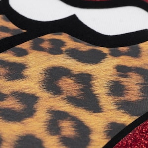Puede incluir: Primer plano de un diseño con estampado de leopardo, detalles en negro y una forma blanca delineada en negro. El fondo es un brillante rojo con purpurina. El diseño es llamativo y vibrante.
