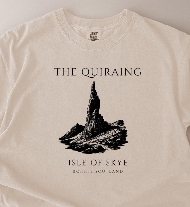 Pode incluir: Camiseta creme com uma ilustra&ccedil;&atilde;o em preto e branco de uma cordilheira. O texto "THE QUIRAING" est&aacute; acima da ilustra&ccedil;&atilde;o, e "ISLE OF SKYE BONNIE SCOTLAND" est&aacute; abaixo.