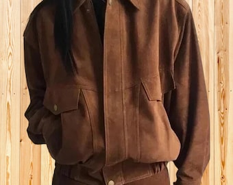 Op de afbeelding: Een bruin suède jack met een klassieke kraag, lange mouwen met knoopmanchetten en twee voorzakken met kleppen. Het jack heeft een centrale knoopsluiting en een gestructureerde zoom, met een uniforme matte textuur over het hele kledingstuk.