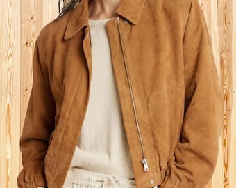 Op de afbeelding: Een beige suède jas met een klassieke kraag, lange mouwen met elastische boorden en een volledige zilverkleurige metalen ritssluiting. De jas wordt gedragen over een crèmekleurige gebreide trui en een lichte broek met trekkoord.