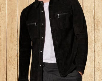 May include: A black suede shirt jacket with two chest pockets and two zippered pockets. The jacket has a button-down front and a collared neckline. The model is wearing a white t-shirt underneath and gray pants.