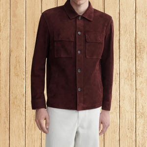 Puede incluir: Chaqueta de ante burdeos con cuello, dos bolsillos en el pecho y cierre de botones. La chaqueta tiene mangas largas y se combina con pantalones blancos. La chaqueta es de color rojo oscuro.