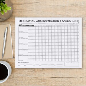 Puede incluir: Un formulario de registro de administraci&oacute;n de medicamentos (MAR) sobre una superficie de madera. El papel blanco tiene una cuadr&iacute;cula para el seguimiento de medicamentos, con secciones para nombre, medicamento, hora y fechas. El t&iacute;tulo "MEDICATION ADMINSITRATION RECORD (MAR)" est&aacute; en la parte superior.