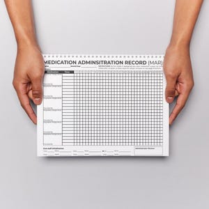 Puede incluir: Un bloc de notas de registro de administraci&oacute;n de medicamentos (MAR) es sostenido por dos manos. El bloc de notas es blanco con l&iacute;neas de cuadr&iacute;cula y texto en negro. El texto "MEDICATION ADMINISTRATION RECORD (MAR)" est&aacute; impreso en la parte superior.