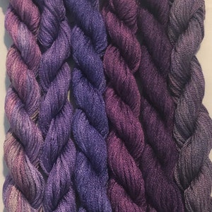 Puede incluir: Cinco madejas de hilo de bordar en tonos de morado, que van desde un lavanda claro hasta un violeta oscuro.