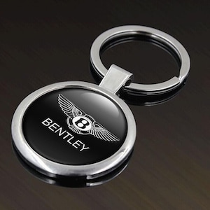 May include: A silver Bentley keyring with a circular black emblem. The emblem displays the Bentley logo and name in white. The keyring has a silver key ring.