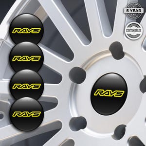May include: Black RAYS wheel centre caps with a yellow logo. The caps have a glossy finish and are set against a silver alloy wheel. The image also shows a 5-year warranty and custom-made badge.