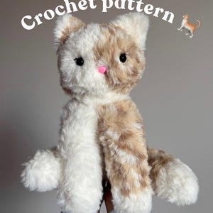 May include: A plush, handmade cat toy with a white and tan color pattern. The cat has black eyes and a pink nose. The words "Crochet pattern" are written above the cat. A small illustration of a cat is also present.