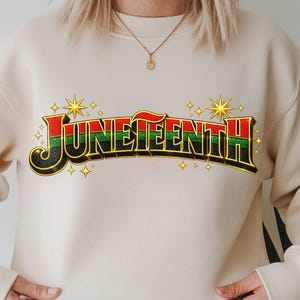 Può includere: Felpa Juneteenth color crema con la scritta "Juneteenth" in un design 3D colorato. Il testo presenta colori rosso, verde e nero con dettagli dorati e stelle. La felpa ha maniche lunghe e girocollo.