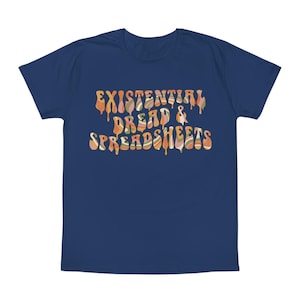 Può includere: T-shirt blu navy con la scritta "EXISTENTIAL DREAD & SPREADSHEETS" in un font retrò a goccia. Il testo è nei toni dell'arancione, del marrone e del verde. È un capo d'abbigliamento casual.