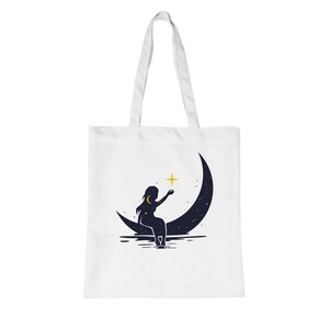 Peut inclure: Sac fourre-tout blanc avec un motif céleste. Une silhouette d'une personne assise sur un croissant de lune, tendant la main vers une étoile jaune. La lune est bleu foncé avec des étoiles blanches. Le sac a des anses blanches.