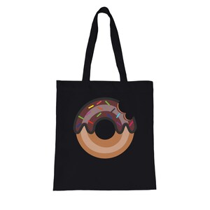 Peut inclure: Sac fourre-tout noir avec un motif de beignet de dessin animé. Le beignet a un glaçage au chocolat et des vermicelles colorés, avec une bouchée. Le sac a deux anses noires.